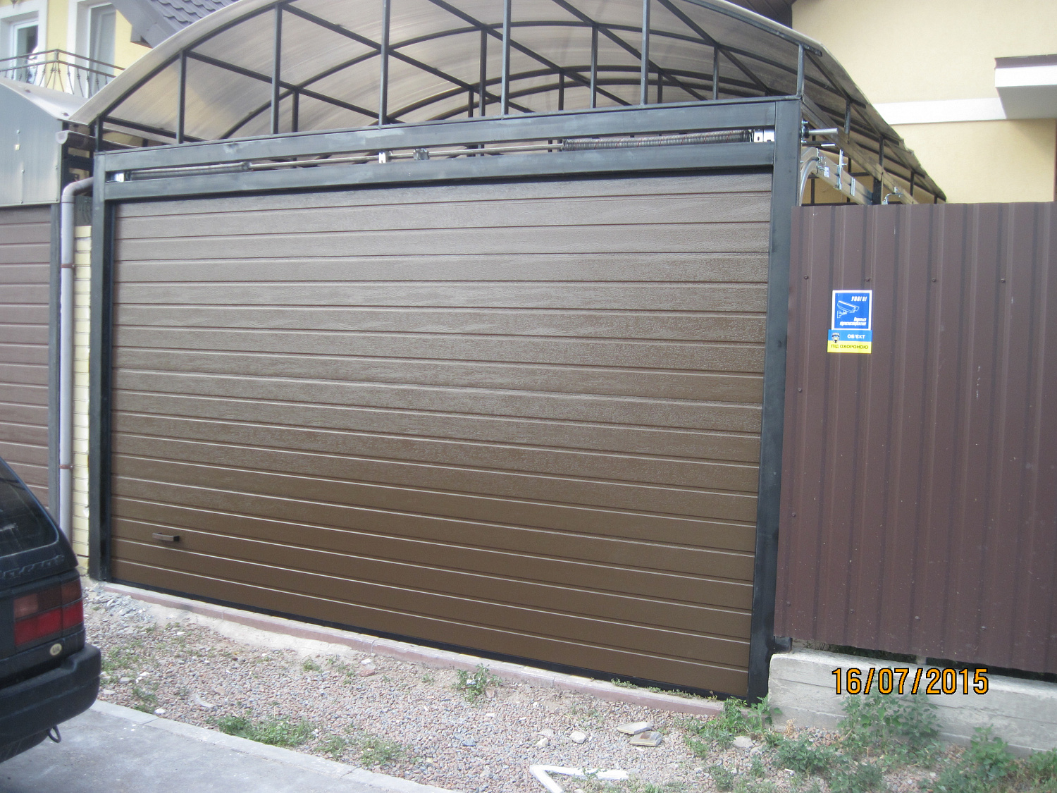 Ворота секційні Алютех під металевим навісом. В'їзд у двір S-гофр RAL 8014.